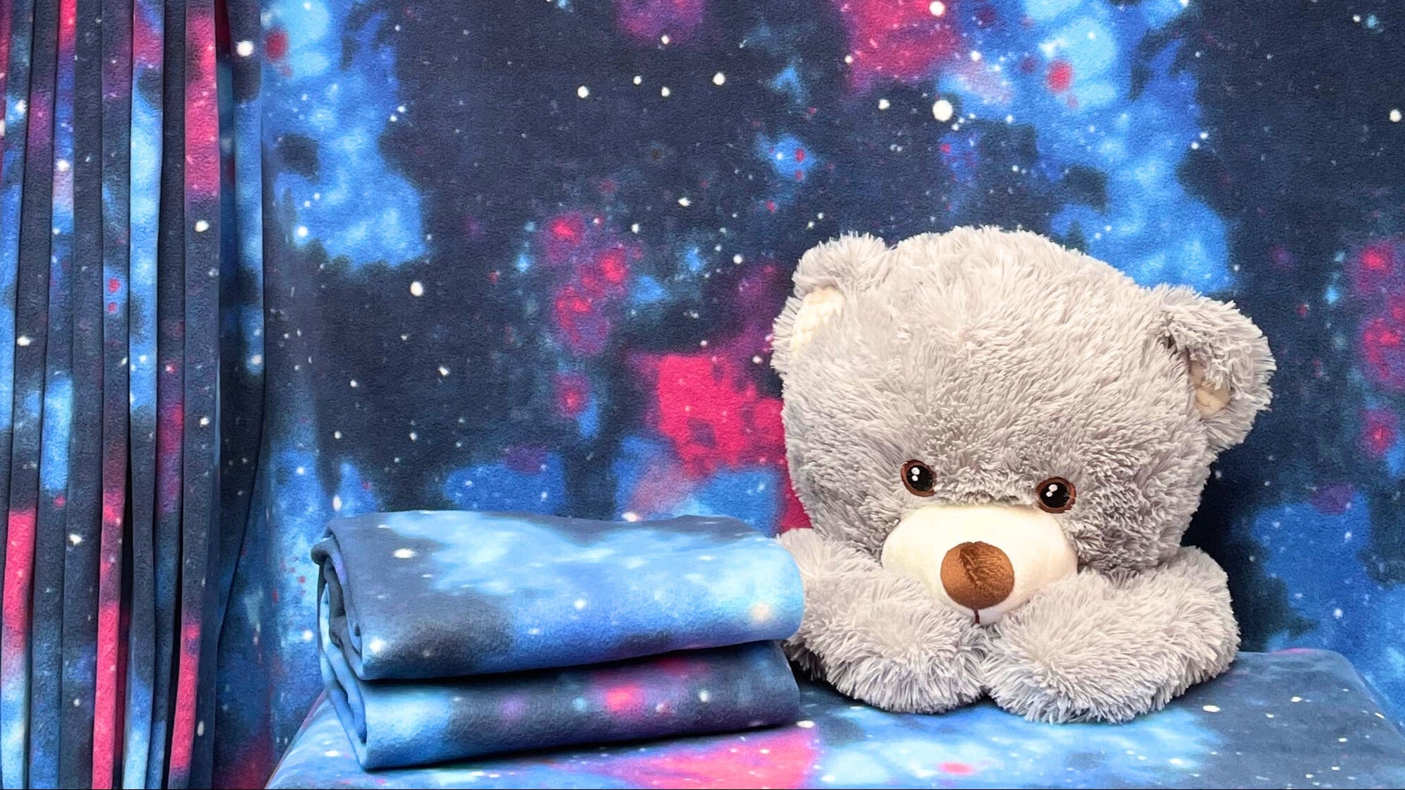 Teddy bear in front of a colorful space-themed curtain
